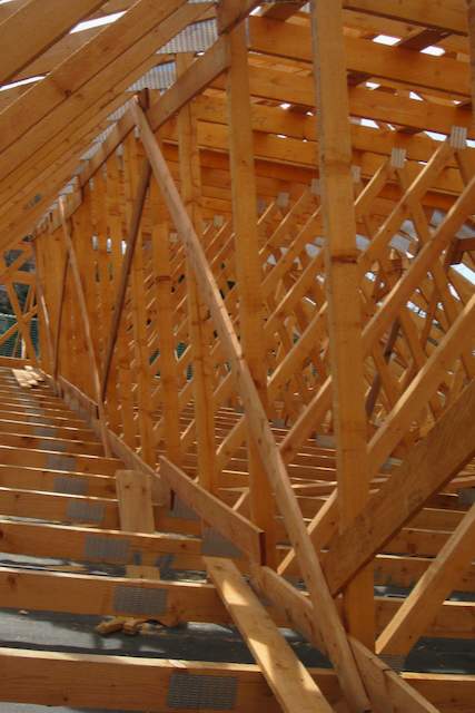 Nahaufnahme von hölzernen Dachstühlen und Balken im Bau, die das Gerüst eines Gebäudes mit sich kreuzenden Hölzern und Metallbefestigungen zeigen, beleuchtet von natürlichem Licht.